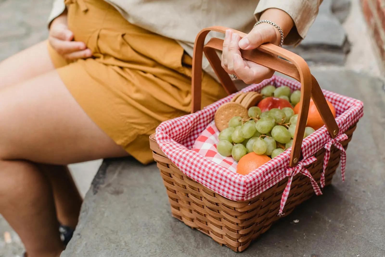 Crop anonymous pregnant female in casual outfit with basket full of fresh ripe fruits and tasty cookies prepared for picnic
