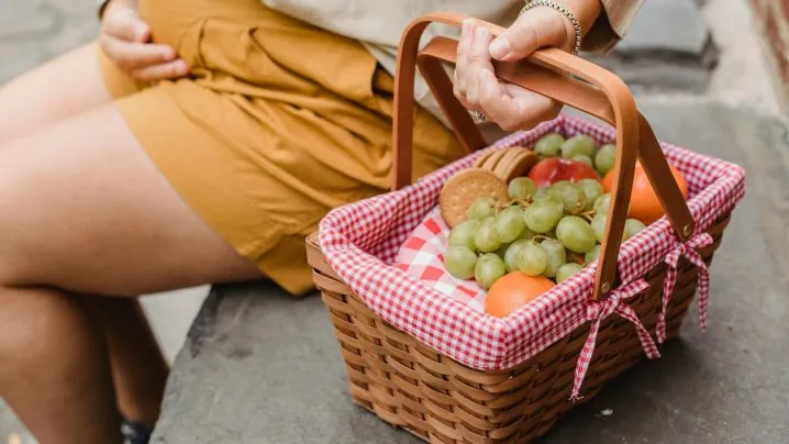 Crop anonymous pregnant female in casual outfit with basket full of fresh ripe fruits and tasty cookies prepared for picnic